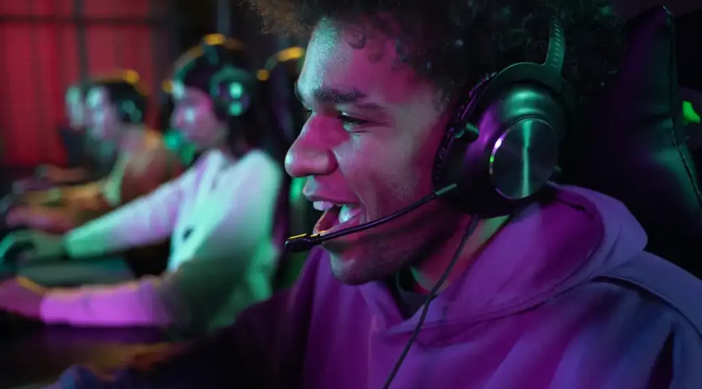 Een esports-speler met een headset speelt geconcentreerd achter een computer. Andere spelers zitten op de achtergrond in dezelfde gamingruimte.