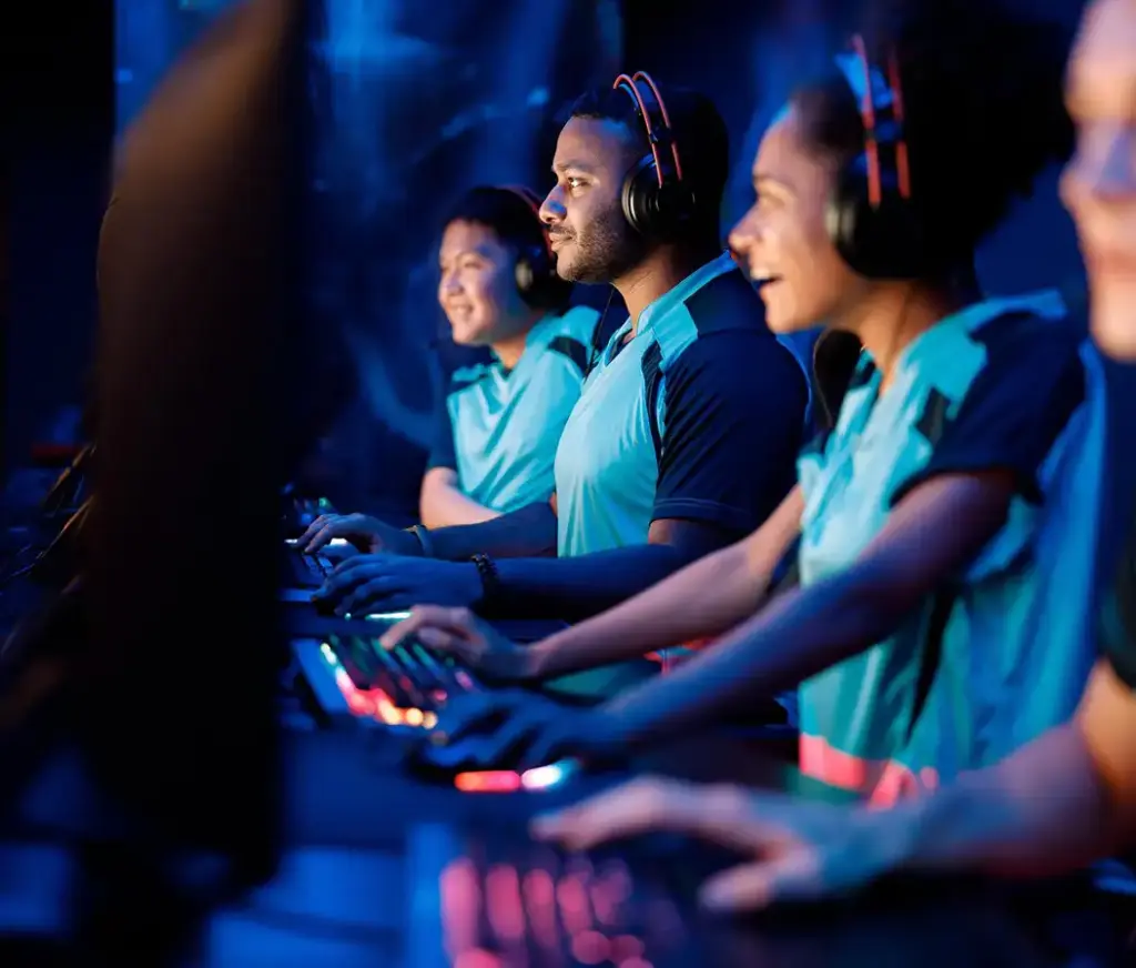 Een team van esports-spelers zit naast elkaar achter gamingcomputers tijdens een wedstrijd. Ze dragen headsets en concentreren zich op het spel in een verlichte esports-arena.