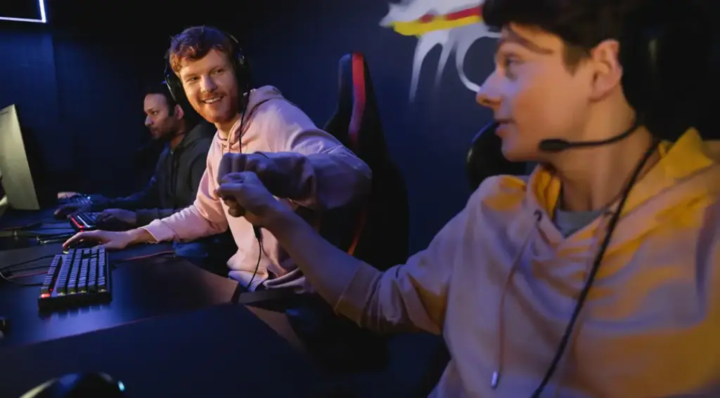 Twee gamers geven elkaar een fist bump tijdens een esportswedstrijd. Ze zitten naast elkaar achter gamingcomputers en dragen headsets.