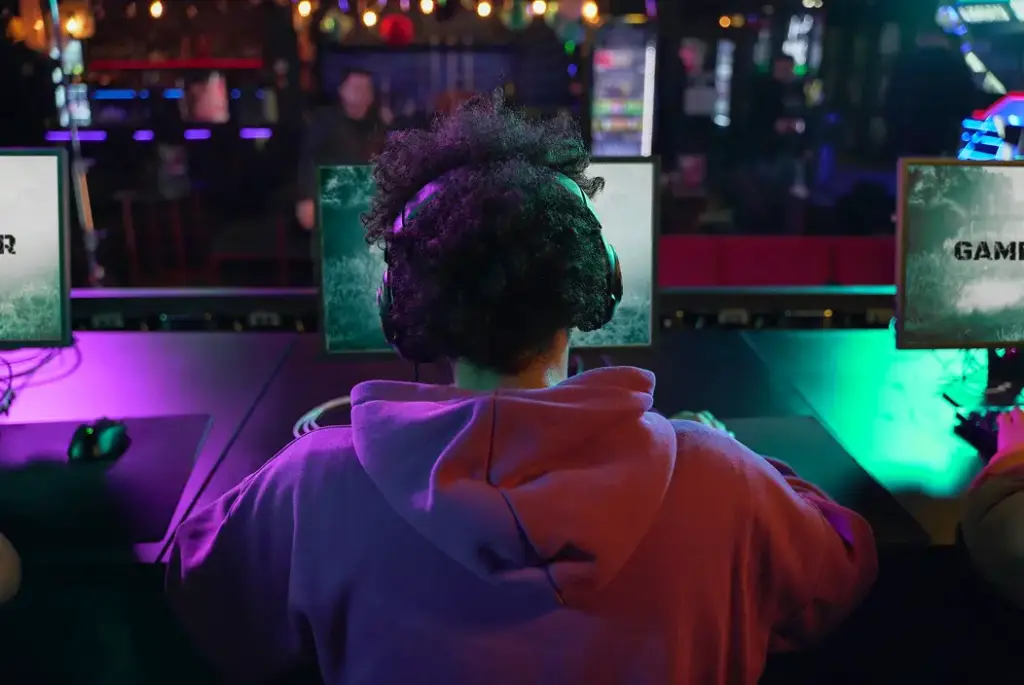 Een gamer zit achter een computer in een esports-arena en kijkt naar het scherm. De gamingruimte is verlicht met neonlichten en meerdere speelstations.