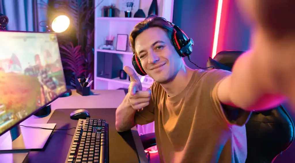 Een gamer met een headset maakt een selfie achter zijn gamingcomputer. Hij zit in een kleurrijke gamingruimte met neonverlichting.